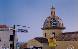 Blau-weiss gekachelte Kirchenkuppel mit gelben Bögen mit Kreuz vor blauem Himmel.